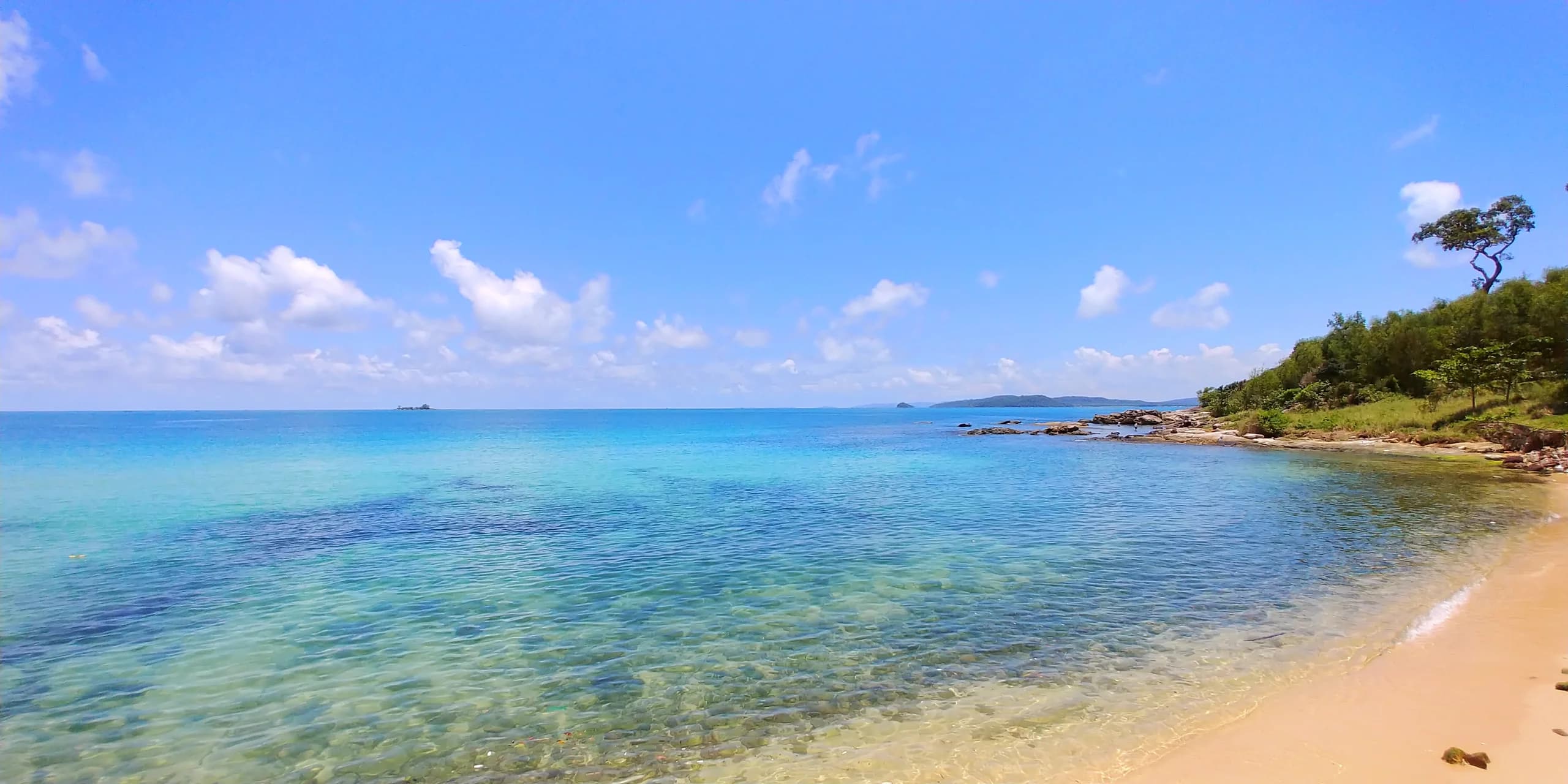 Clear shallow water beside the sandy Vũng Bầu shore and rocky headland