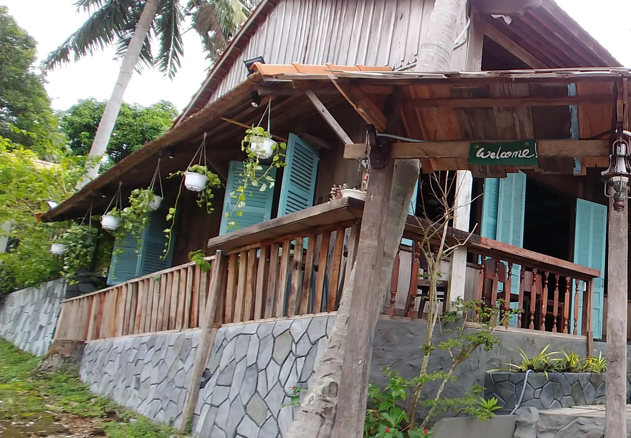 Wooden veranda, turquoise shutters and tropical planting at Xom Cafe