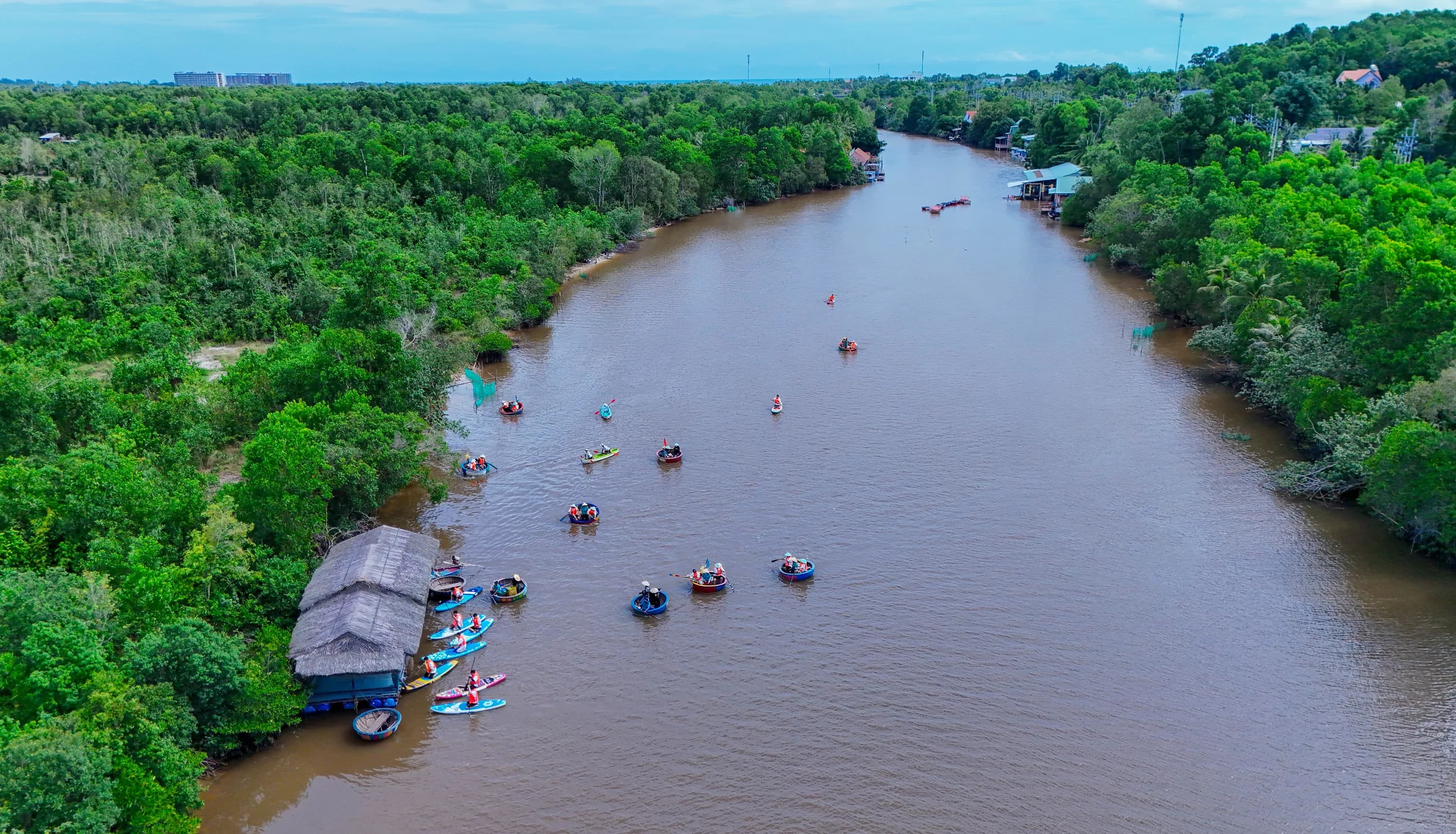 Aerial view along Cua Can River with wooded banks and distant small boats