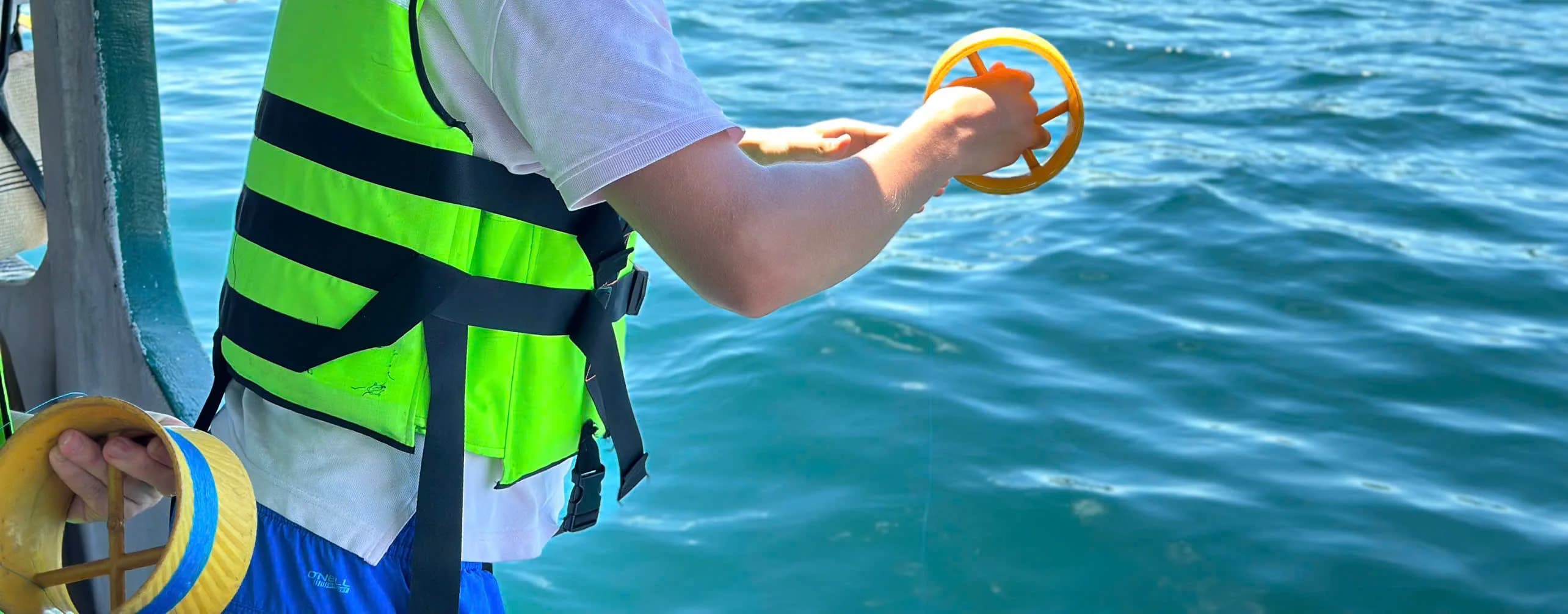 Hands holding a yellow handline reel beside a tour boat rail