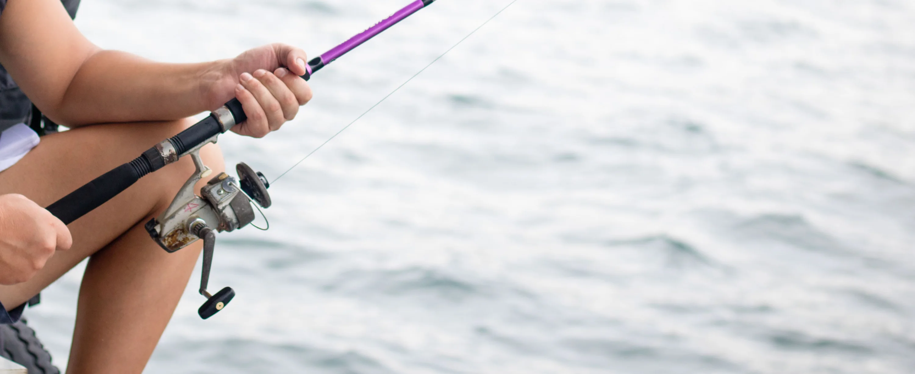 Hands holding a fishing rod and spinning reel over the sea