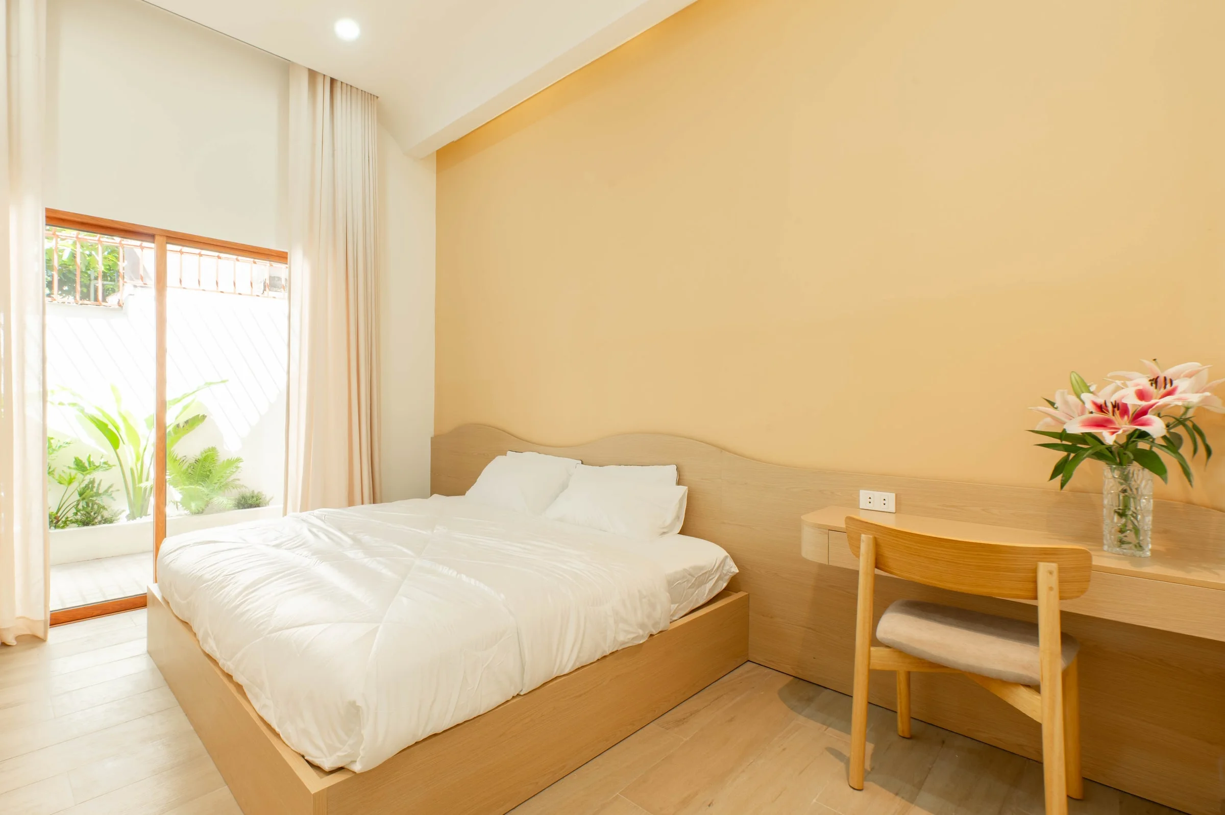 A bright guest bedroom with a desk beside a garden-facing window