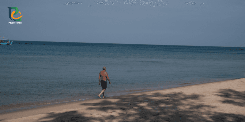 Tourist walking along shoreline at Truong Beach Phu Quoc with calm clear water for swimming