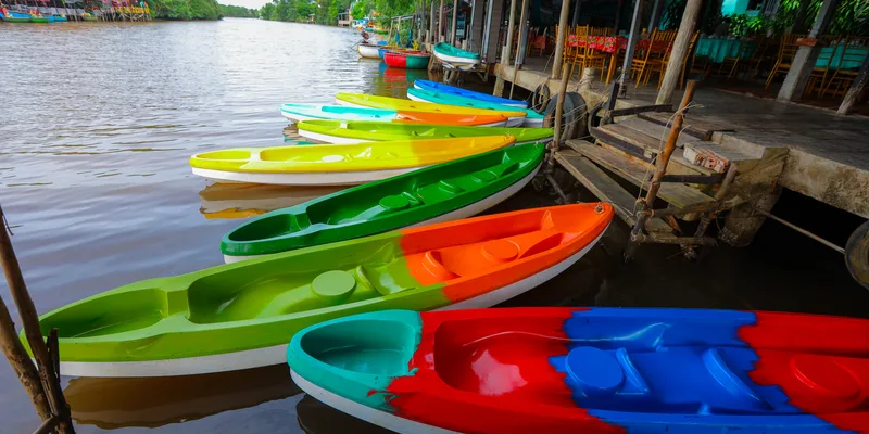 A row of empty kayaks beside a shaded Cua Can riverside landing